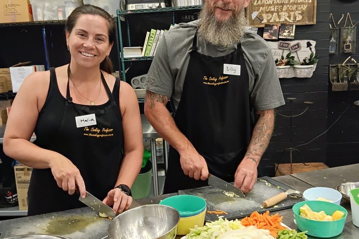 Two people preparing food in a kitchen with vegetables on the counter.