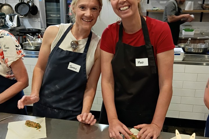 Two women in aprons smiling while preparing food in a kitchen.