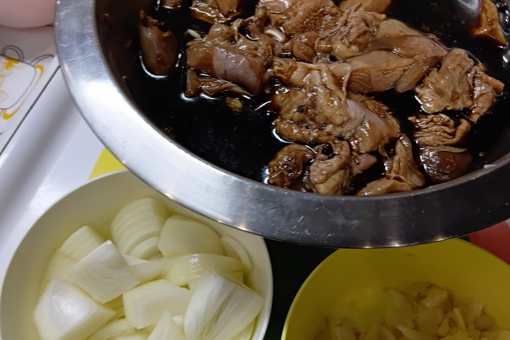 Marinated meat in a bowl with chopped onions and garlic in separate bowls.
