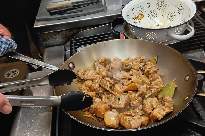 Person cooking meat in a pan with tongs, kitchen setting.