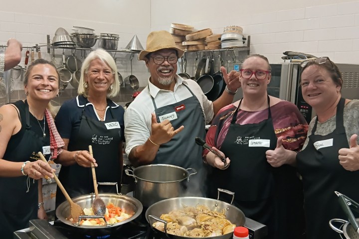 Group in a kitchen cooking together, smiling, with pans on the stove.