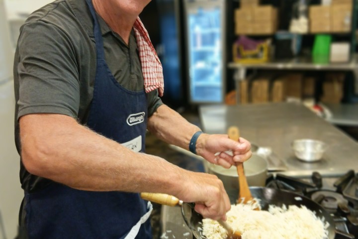 Man in apron cooking rice in a pan on a stove.