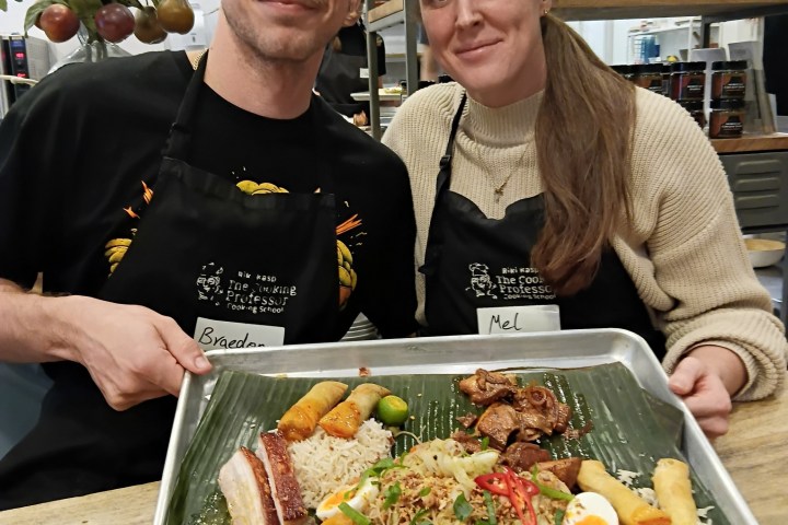 Two people holding a tray with a variety of food on a banana leaf.