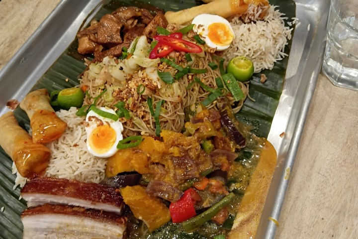 Assorted Asian dishes with rice, vegetables, and spring rolls on a metal tray.
