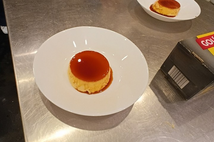 Two plates of caramel flan on a metal table.