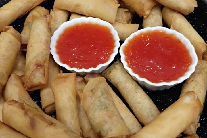 A plate of spring rolls with two small bowls of red sauce.