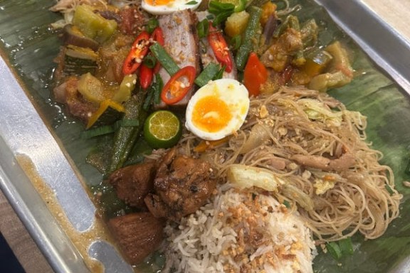 Platter with rice, noodles, boiled eggs, vegetables, and meats on a banana leaf.