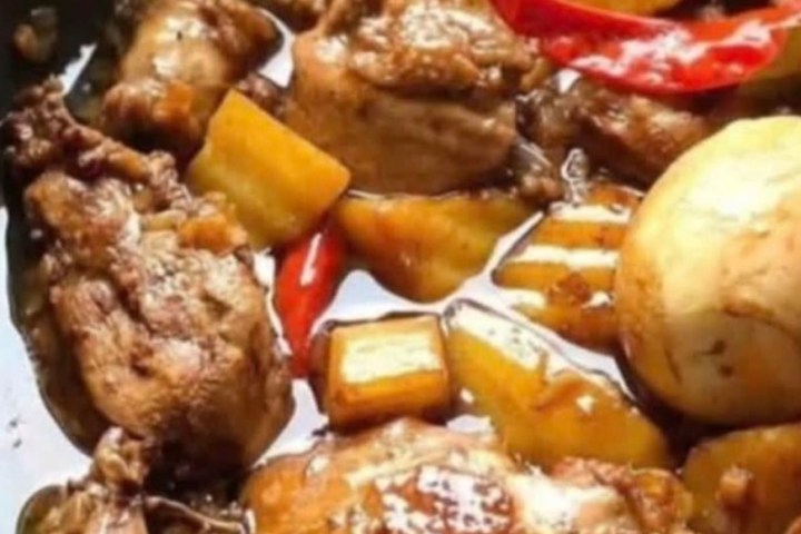 Close-up of cooked chicken pieces with peppers and potatoes in a pan.