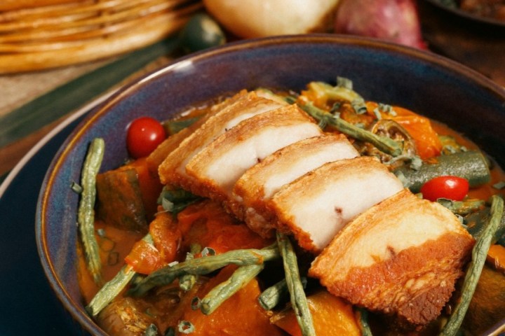 Blue bowl with sliced roasted pork belly on mixed vegetables.