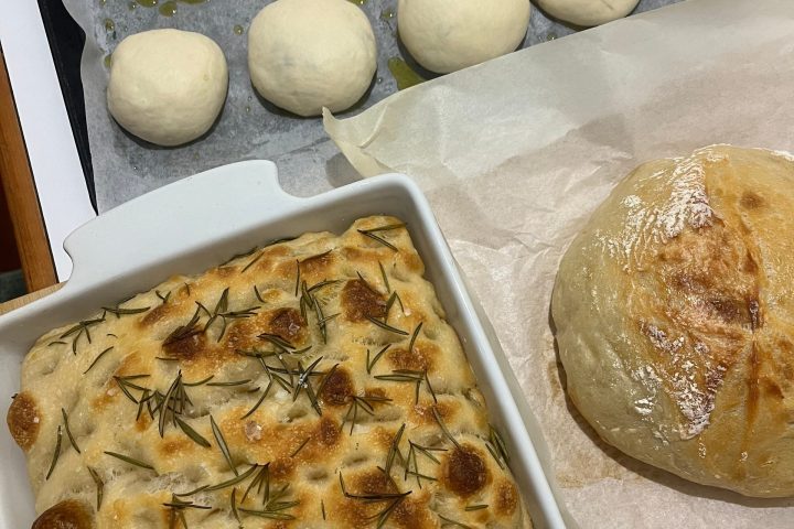 Dough balls, rosemary focaccia, and a round loaf on parchment paper.