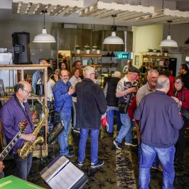 Musicians playing guitar and saxophone at a lively gathering in a cafe setting.