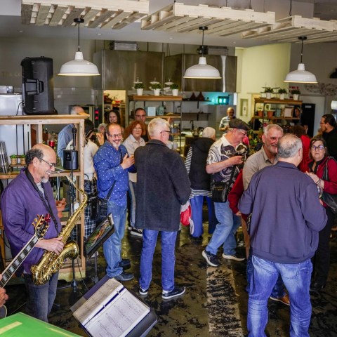 Musicians playing guitar and saxophone at a lively gathering in a cafe setting.