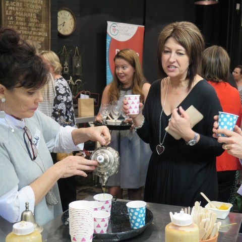 Woman pours tea into cups at a social gathering with others holding paper cups.