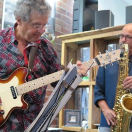Two musicians playing guitar and saxophone indoors.