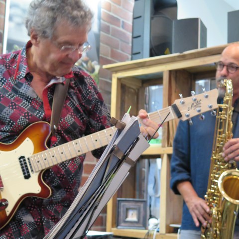 Two musicians playing guitar and saxophone indoors.