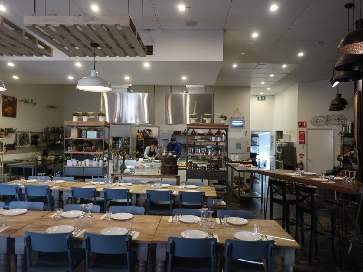 Spacious restaurant interior with tables set, open kitchen, and modern decor.