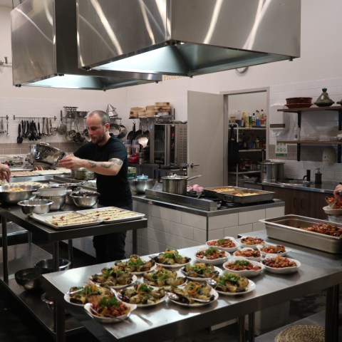 Three chefs preparing dishes in a commercial kitchen with various plates on tables.