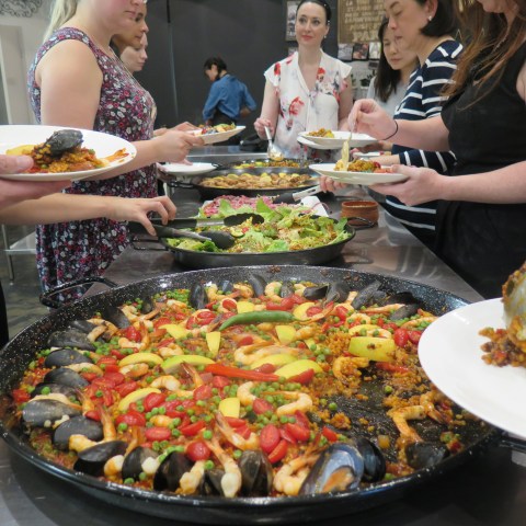 People serving themselves various dishes, including paella, from a buffet table.