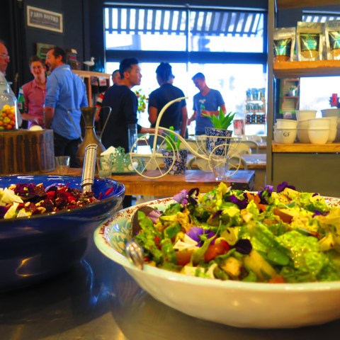 Two salad bowls on a counter in a cozy café with customers in the background.