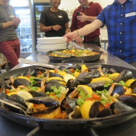 A large pan of seafood paella on a table with people in the background.