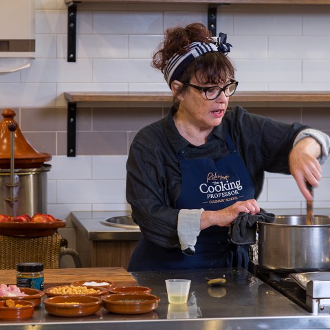 Chef stirring a pot at a cooking class with ingredients on the counter.