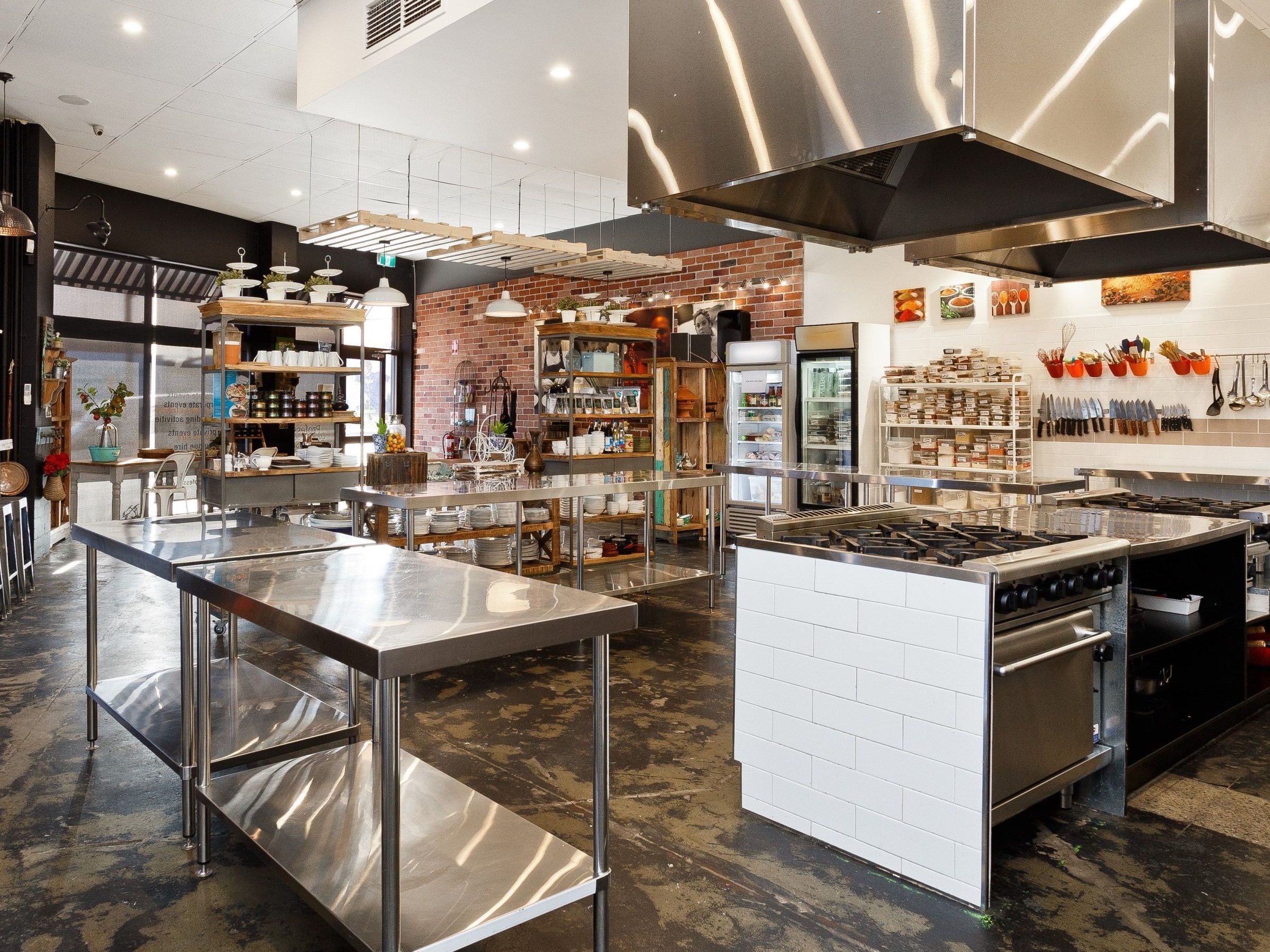 Modern industrial kitchen with stainless steel counters, shelves, and cooking equipment.