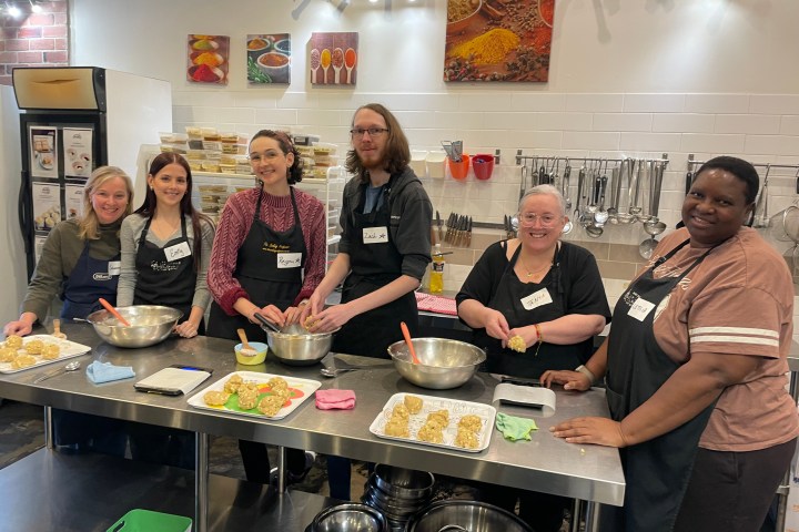 Group cooking class with six people preparing dishes in a kitchen.