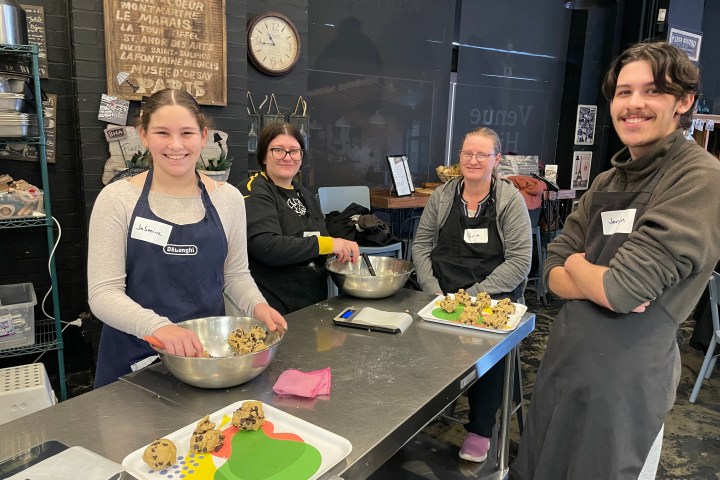 Four people smiling while preparing food at a kitchen counter.