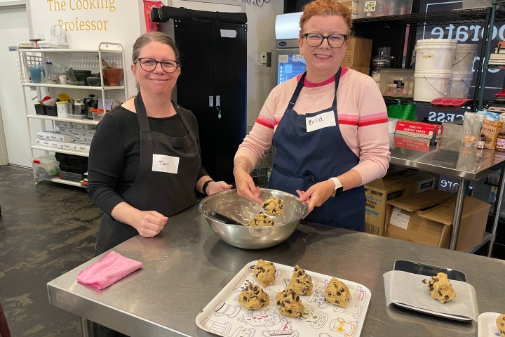 Two women in a kitchen making cookies with chocolate chips.