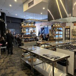 A modern commercial kitchen with stainless steel counters and shelves, people in the background.