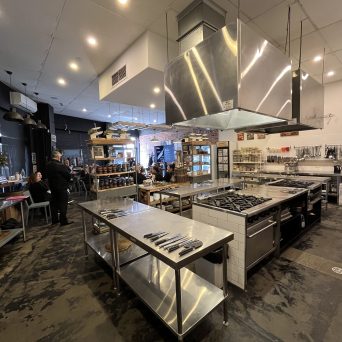 Commercial kitchen with stainless steel appliances and cooking stations.