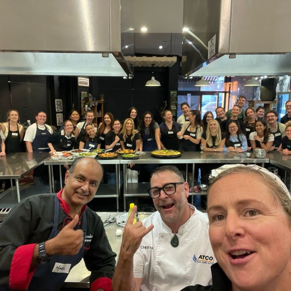 Group of people in a kitchen, posing for a photo around a table with food.